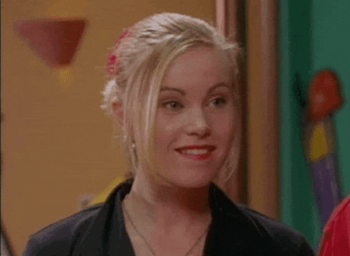 a woman is smiling and looking at the camera while standing in front of a group of people .