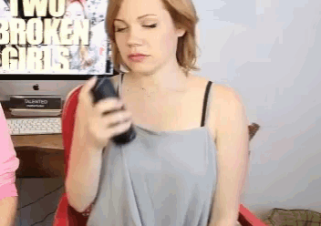 a woman holding a cell phone in front of a sign that says " two broken girls "