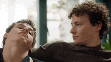 two men with curly hair are sitting next to each other on a couch
