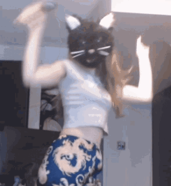 a woman wearing a cat mask is dancing in a room with her arms in the air .