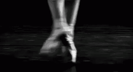 a black and white photo of a ballerina 's feet in pointe shoes dancing on a stage .