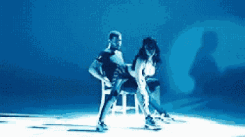 a man and a woman are dancing on a stage while the woman is sitting on a chair .