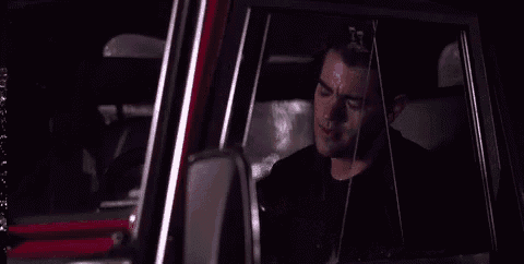 a man is sitting in a car at night looking out the window .