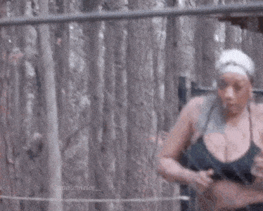 a woman in a black bra and a white headband is standing in front of a chain link fence .