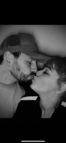 a man and a woman are kissing in a black and white photo . the man is wearing a hat .