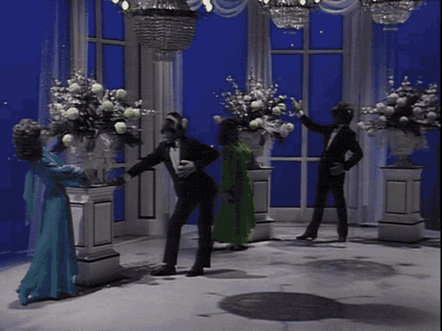 a man in a tuxedo and a woman in a green dress are dancing in a room