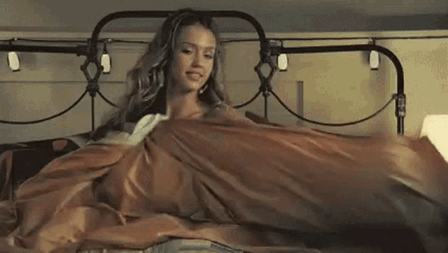 a woman is laying in a bed with a lamp and a blanket .