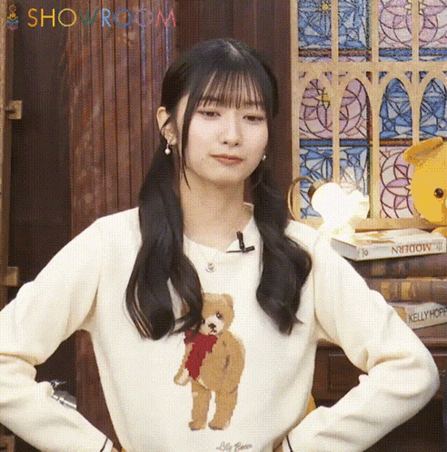 a woman wearing a white sweater with a teddy bear on it is standing in front of a showroom sign