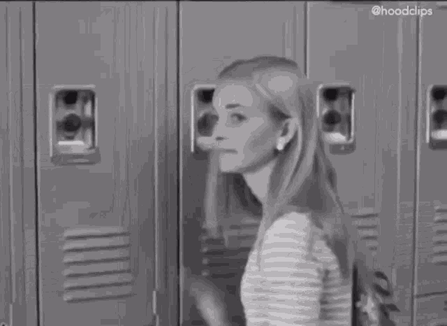 a girl is standing in front of a row of lockers in a black and white photo .