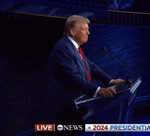 a man in a suit and tie stands at a podium with a live abc news headline