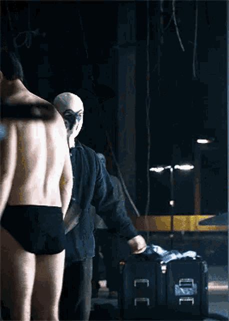 a shirtless man in black underwear is standing next to a man in a mask .
