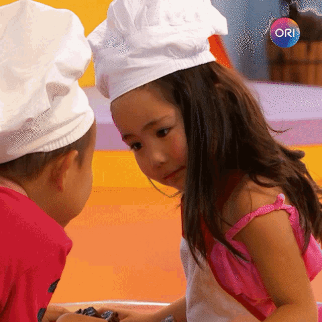 a little girl wearing a chef hat looks at a boy wearing a chef hat