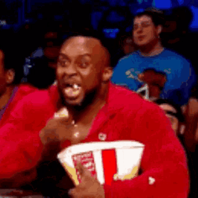 a man in a red shirt is eating popcorn in a crowded room .