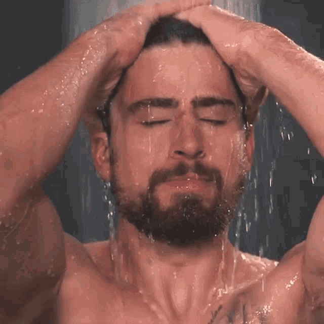 a shirtless man with a beard is taking a shower