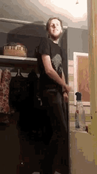 a man in a black shirt is standing in a closet with a spray bottle