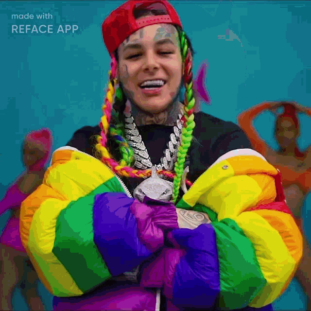 a man with a rainbow jacket and a red hat is smiling with his arms crossed