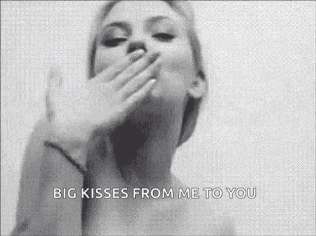 a woman is blowing a kiss and covering her mouth with her hand in a black and white photo .