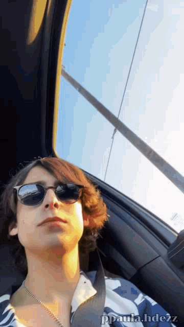 a young man wearing sunglasses is sitting in a car looking out the window ..