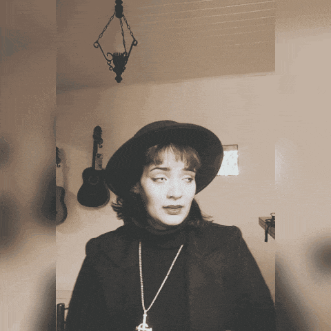 a woman wearing a hat and a necklace stands in front of a guitar