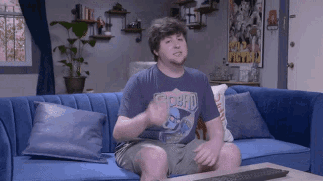 a man is sitting on a blue couch wearing a shirt that says chobad