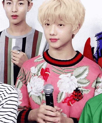 a young man in a pink sweater is holding a microphone in his hands .