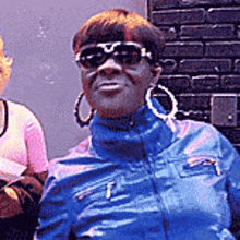 a woman wearing sunglasses and hoop earrings is standing next to another woman .