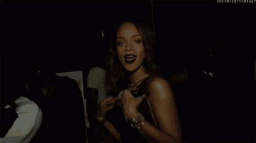a woman in a black dress is dancing in a dark room with a group of people .