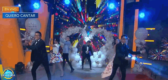 a group of people are dancing on a stage with balloons and fireworks in the background