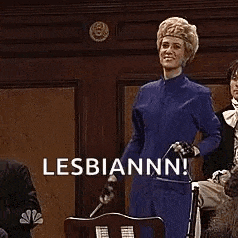 a woman in a blue suit is sitting in a chair holding a sword and the words lesbiannn .