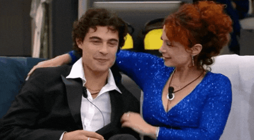 a man in a tuxedo and a woman in a blue dress are sitting next to each other on a couch