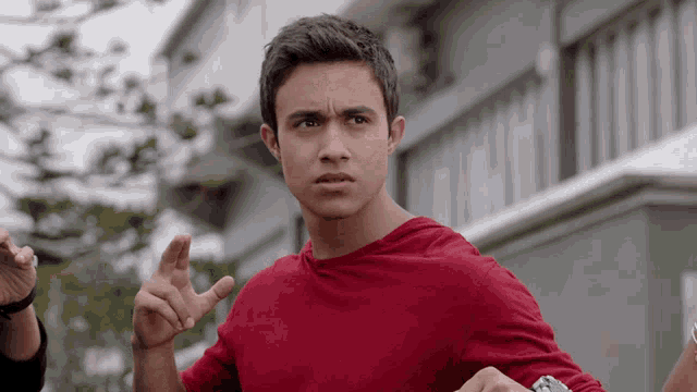 a young man in a red shirt is making a hand gesture
