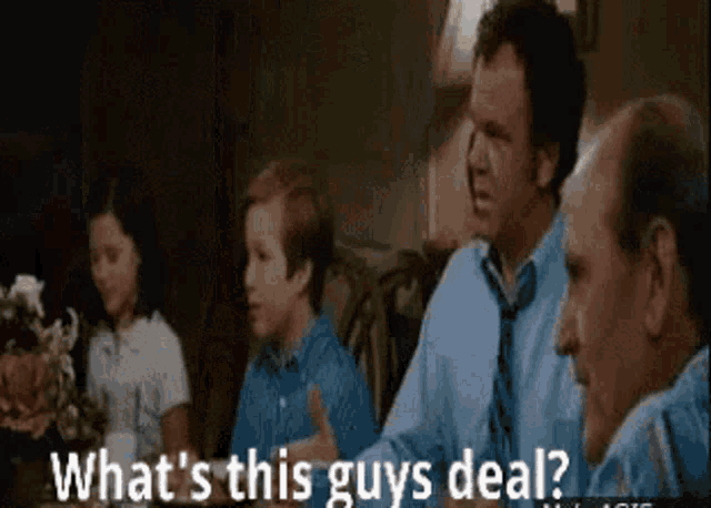 a group of people are sitting at a table and one of them is asking what 's this guys deal ?