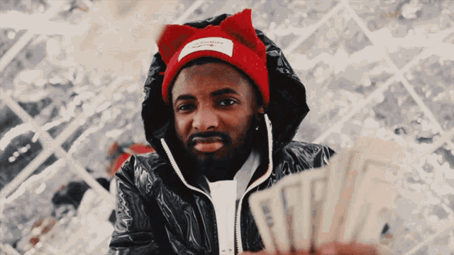 a man wearing a red cat ear hat is holding a stack of money