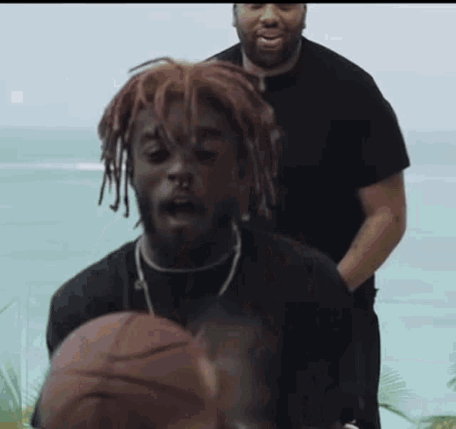 a man with dreadlocks is holding a basketball in his hand while another man stands behind him .
