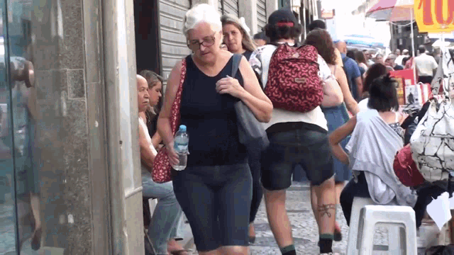 a woman carrying a bottle of water walks down a busy street