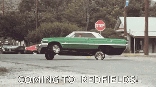 a green lowrider car is driving down a street with a stop sign in the background