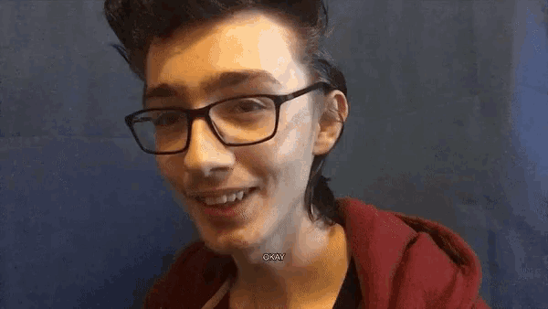 a young man wearing glasses and a red hoodie is smiling and says okay