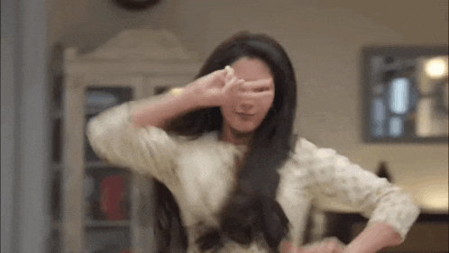 a woman is covering her eyes with her hand while dancing in a living room .