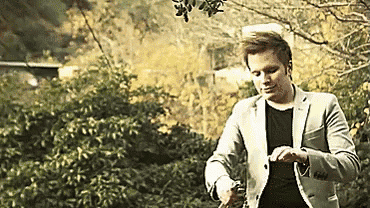 a man in a suit is standing in a park looking at his watch .