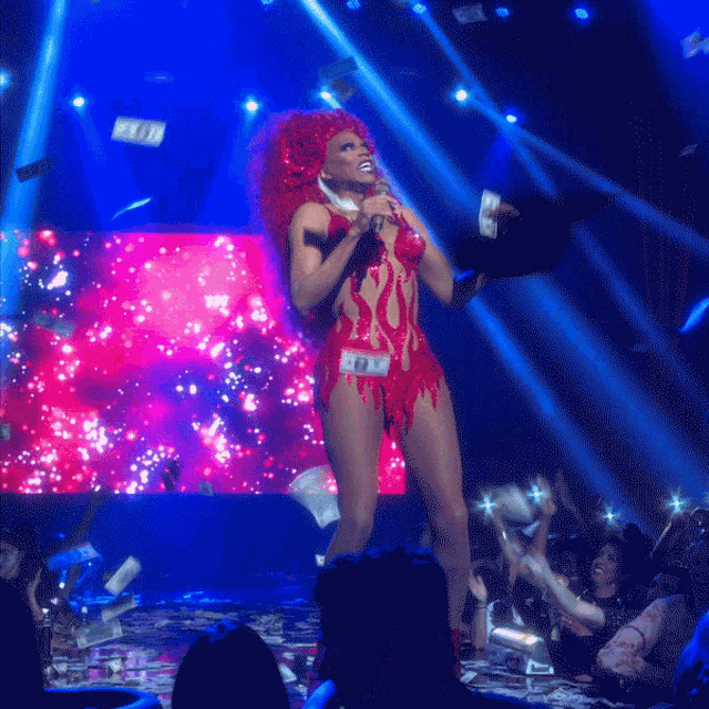 a woman in a red costume is singing into a microphone while money is falling around her