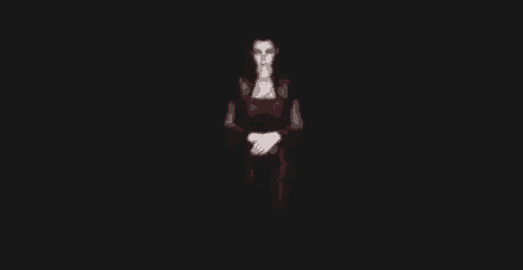 a woman in a red dress is standing in a dark room with her hands folded .