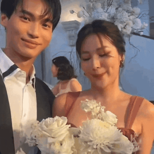 a man and a woman are posing for a picture while the woman is holding a bouquet of white flowers .
