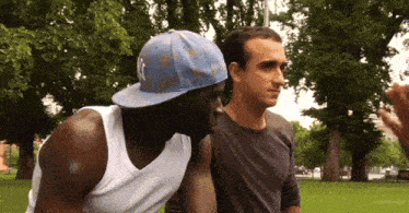 a man wearing a white tank top and a blue hat with the letter k on it