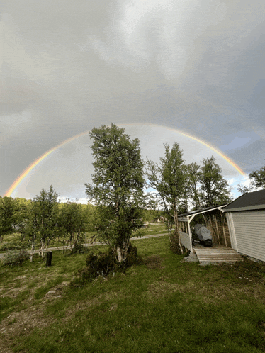 a rainbow is visible over a house and a shed