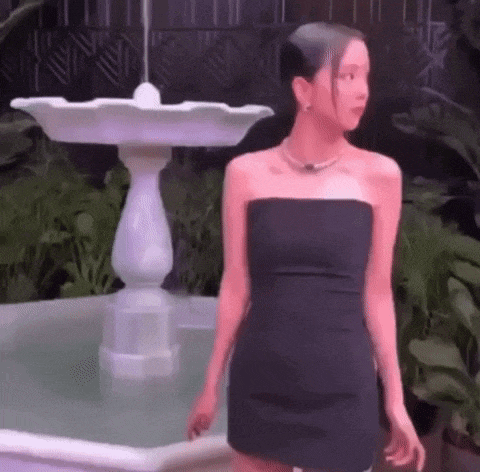 a woman in a strapless black dress is standing in front of a fountain .