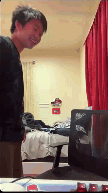 a man is standing in front of a bed with a red curtain behind him