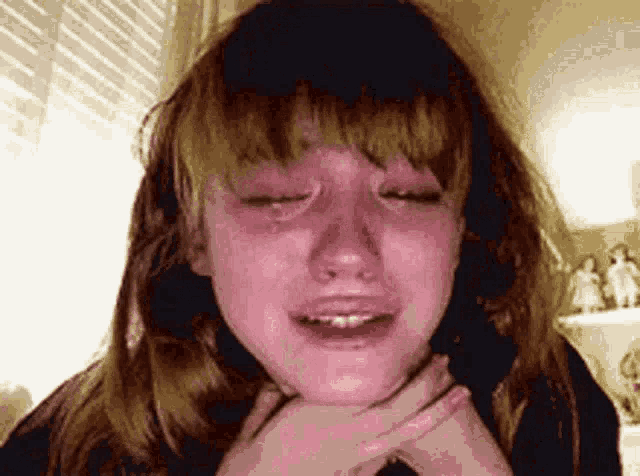 a girl is crying with her eyes closed and her hands on her neck .