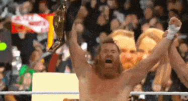 a bearded man is holding a wrestling championship belt in the air .