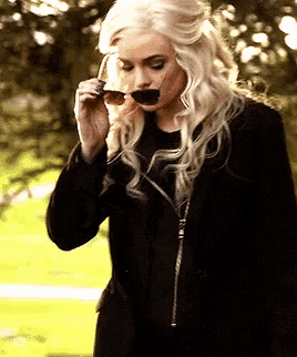 a woman in a black coat is holding a pair of sunglasses in her mouth