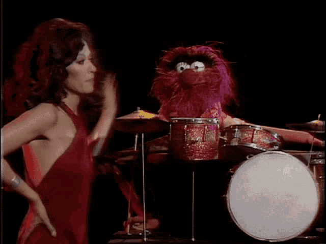 a woman in a red dress stands next to a drummer